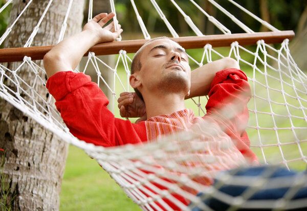 man laying down on a hammock in a tropical home's garden