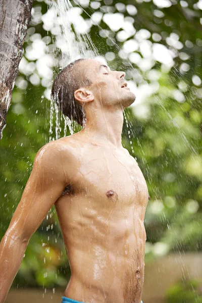 Jovem atraente desfrutando de um chuveiro em um jardim tropical com palmeiras — Fotografia de Stock