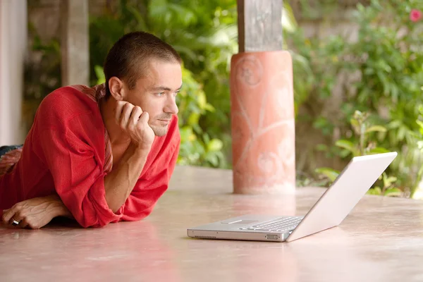 Hombre atractivo usando una computadora portátil mientras está acostado —  Fotos de Stock