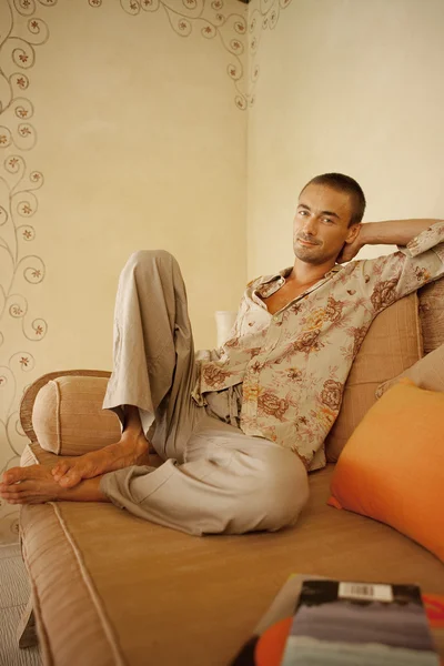 Homme attrayant assis sur un canapé avec des livres pendant les vacances . — Photo