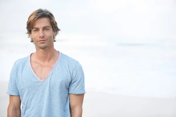 Genç çekici bir adam sahilde deniz arka planda — Stok fotoğraf