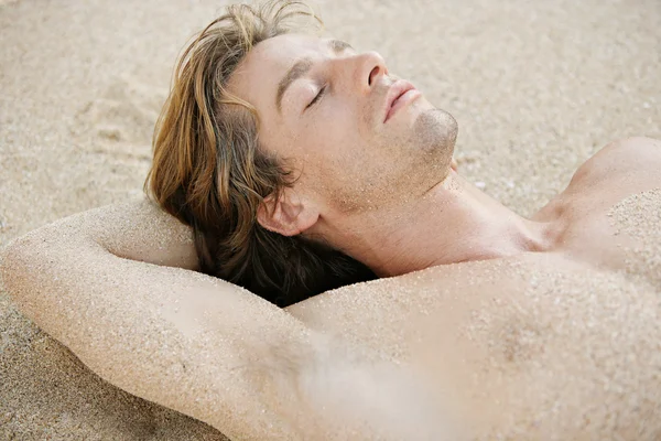 Attraente giovane uomo che dorme su una spiaggia di sabbia dorata . — Foto Stock