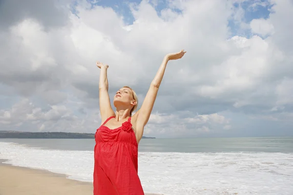 Aantrekkelijke jonge vrouw die zich uitstrekt haar armen omhoog wile staande op een gouden zandstrand. — Stockfoto