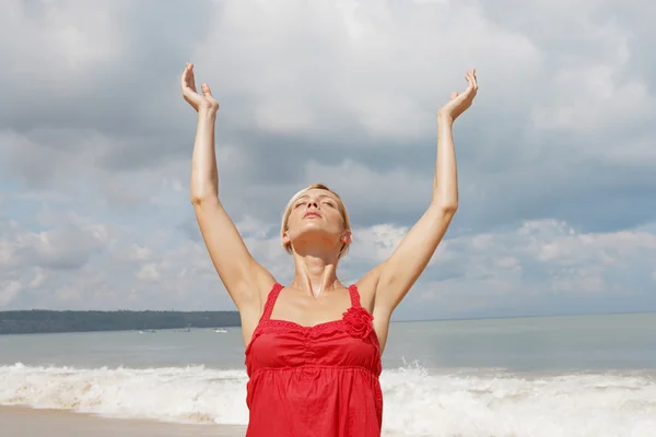 Attrayant jeune femme étirant ses bras vers le haut wile debout sur une plage de sable doré . — Photo