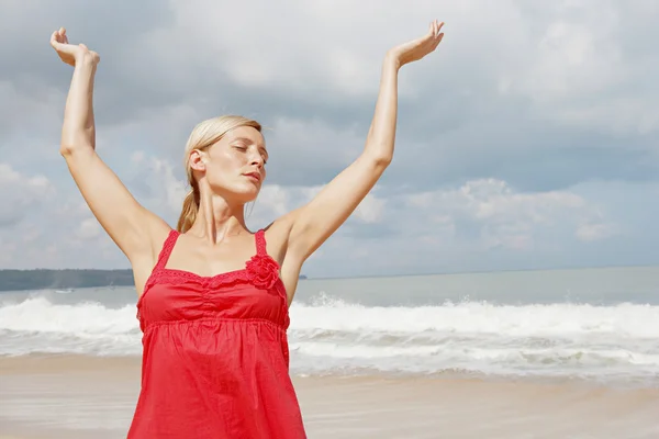 Attraktive junge Frau, die ihre Arme in die Höhe streckt und am goldenen Sandstrand steht. — Stockfoto