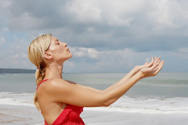 Młoda kobieta trzymając ręce razem stojąc na plaży burzliwy niebo. — Zdjęcie stockowe