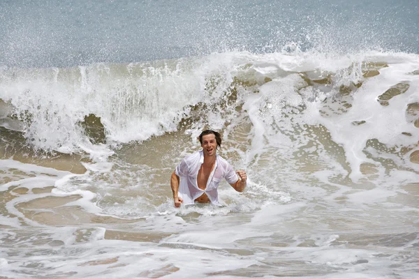 Jeune homme attrayant courant hors de l'océan sauvage, avec une grande vague le frappant . — Photo