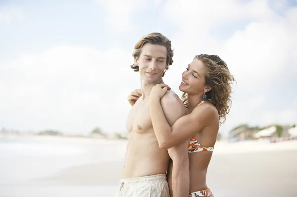 Giovane donna attraente abbracciare l'uomo da dietro mentre in piedi su una spiaggia di sabbia bianca . — Foto Stock