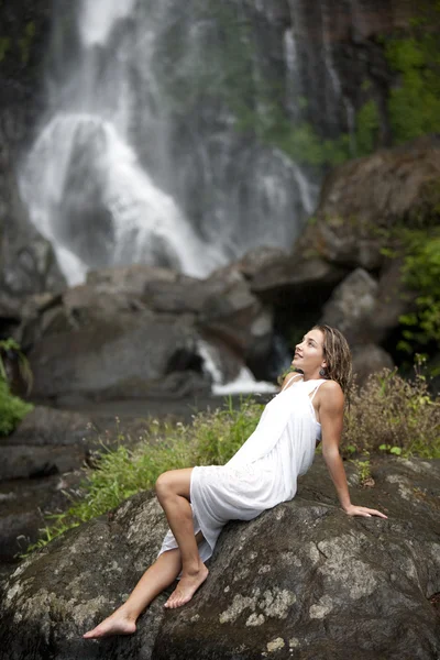 Junge Frau setzt sich auf Felsen bei Wasserfällen. — Stockfoto