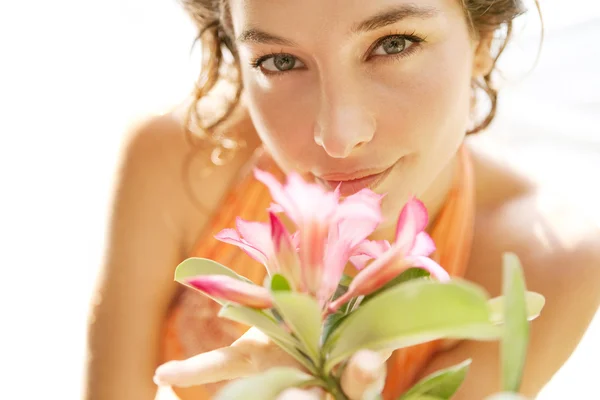 Jovem menina atraente cheirando uma flor rosa tropical — Fotografia de Stock