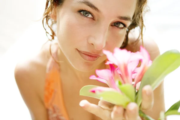 Jovem menina atraente cheirando uma flor rosa tropical — Fotografia de Stock