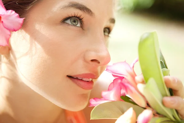 Junges attraktives Mädchen, das eine tropische rosa Blume riecht — Stockfoto