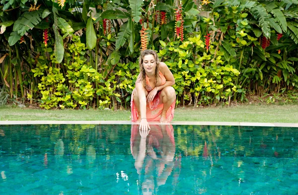 Mujer agachada junto a la piscina y tocando el agua . — Foto de Stock