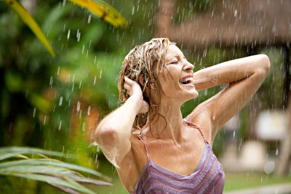 Retrato de uma bela mulher desfrutando de chuva tropical caindo sobre ela em um jardim exótico . — Fotografia de Stock