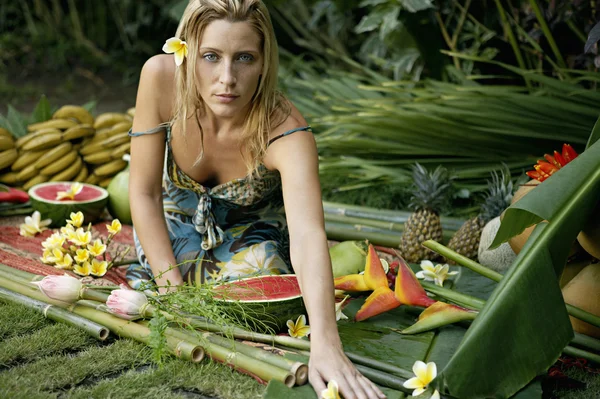 Ung kvinna sitter på en bädd av tropiska frukter i en exotisk trädgård. — Stockfoto