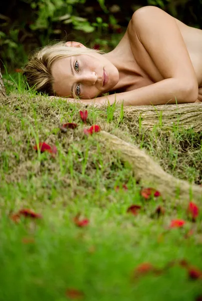 Beautiful blonde woman laying naked on green grass and tree roots — Stock Photo, Image