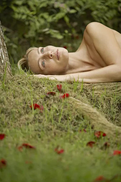 Jovem mulher nua que estabelece na grama verde e pétalas de rosa vermelha — Fotografia de Stock