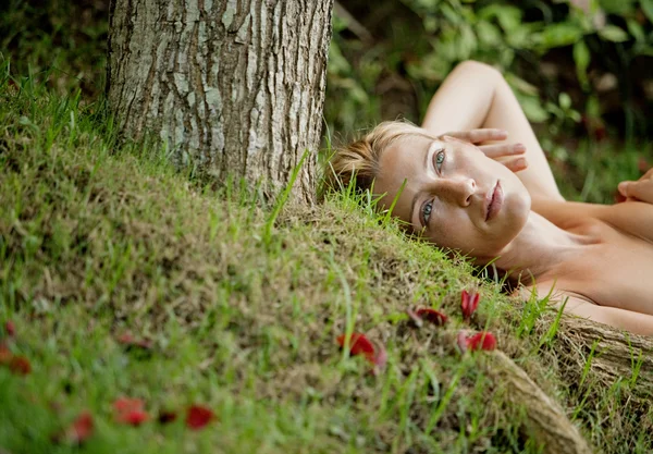 Bela mulher loira deitada nua na grama verde e raízes de árvores — Fotografia de Stock