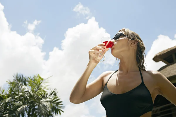 Junge attraktive Frau trinkt einen Cocktail gegen den blauen Himmel. — Stockfoto