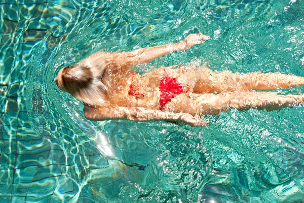 Vista trasera sobre la cabeza de una atractiva joven nadando bajo el agua y usando un bikini rojo mientras está de vacaciones . —  Fotos de Stock