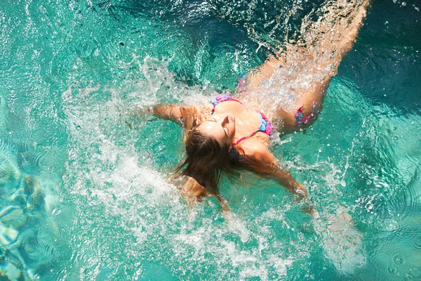 Mujer atlética joven sumergiéndose en una piscina azul, salpicando agua a su alrededor . —  Fotos de Stock