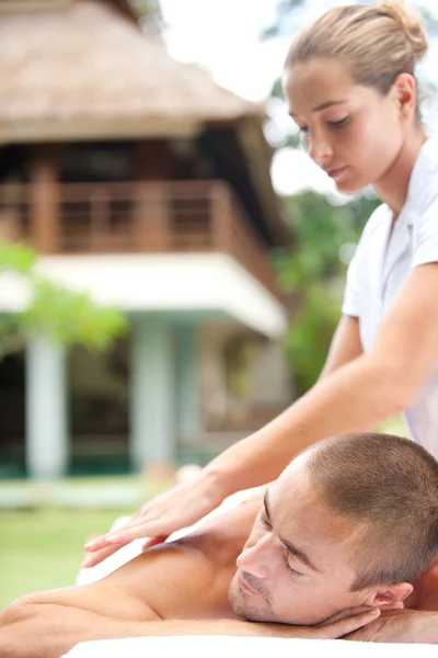 Joven masajista masajeando a un hombre atractivo en un jardín de hotel tropical . — Foto de Stock