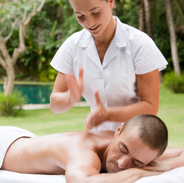 Jonge masseuse masseren een aantrekkelijke man in een tropische tuin in de buurt van een zwembad. — Stockfoto