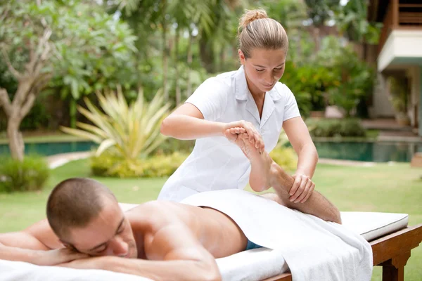 Young masseuse massaging and stretching the body of an attractive man in a tropical hotel garden — Stock Photo, Image