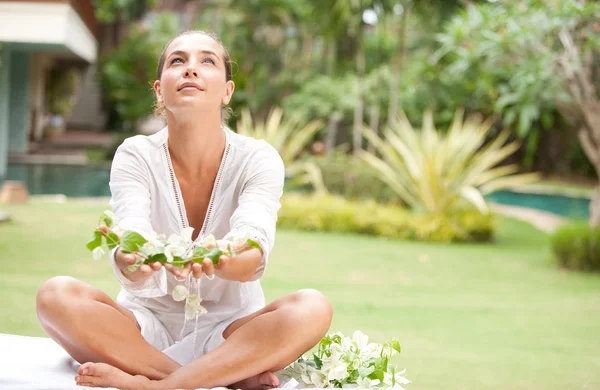 Jovem atraente oferecendo e segurando flores tropicais em suas mãos, em um exótico jardim de spa . — Fotografia de Stock