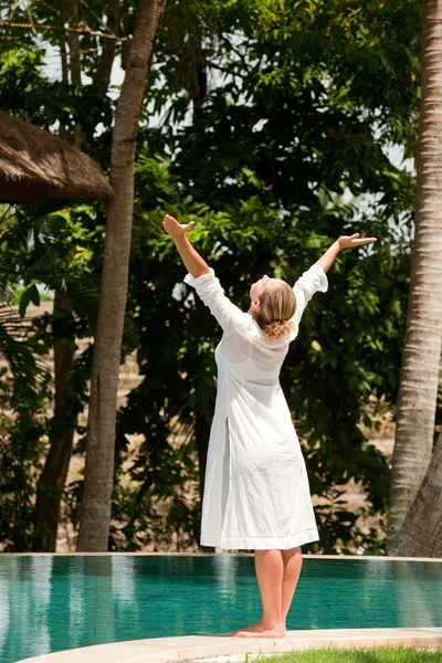 Young woman's figure with arms outstretched while standing at the edge of a swimming pool in a tropical nature location. — Stock Photo, Image