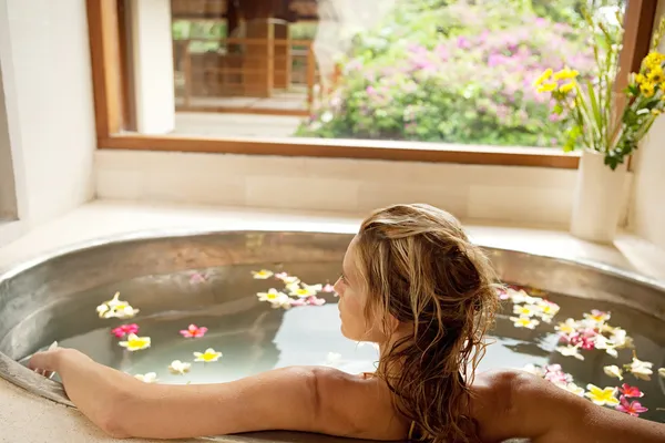 Vista posteriore di una giovane donna che fa il bagno nel bagno di fiori di una spa termale . Foto Stock Royalty Free