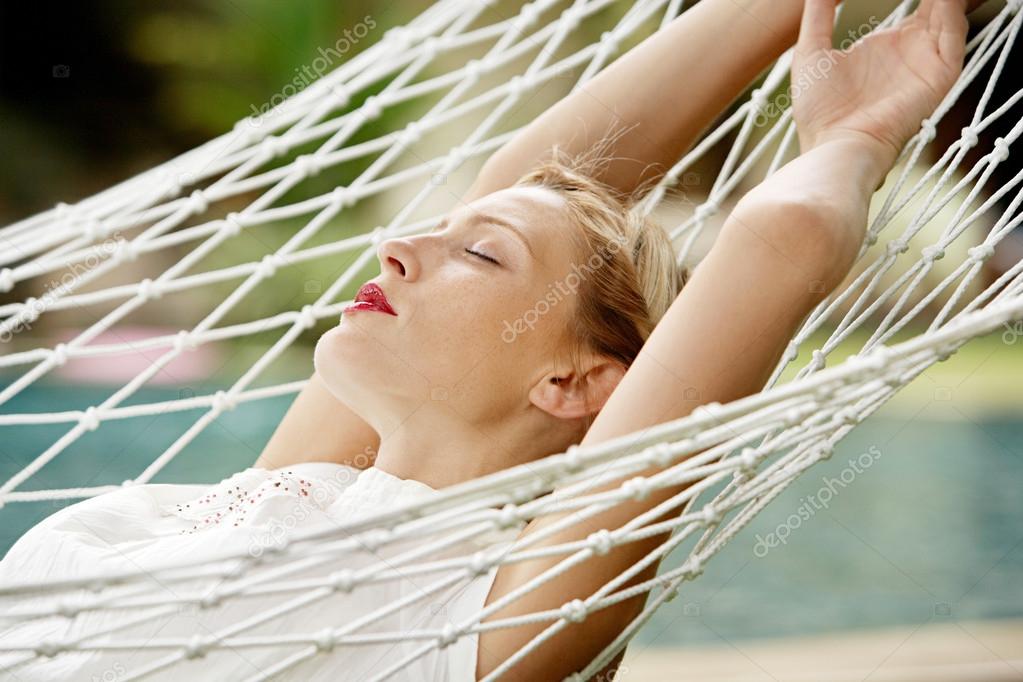 Young attractive woman with red lipstick laying down on a white hammock
