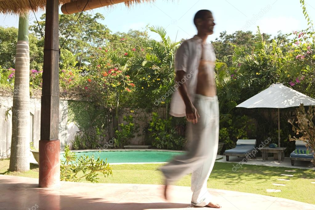 Blurred figure of man walking along an exotic garden with swimming pool.