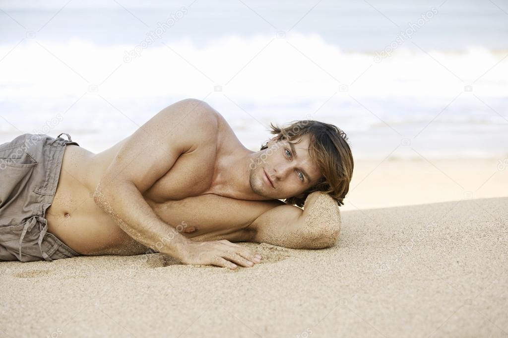 Attractive young man laying down on the beach shore