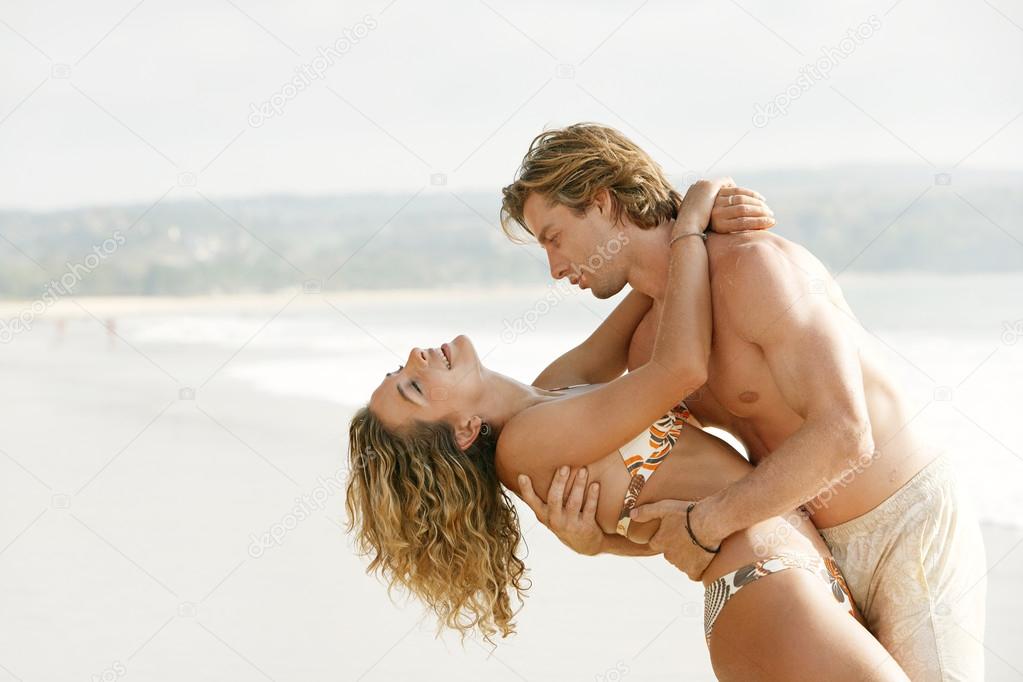 young couple being playful and romantic on a golden sand beach