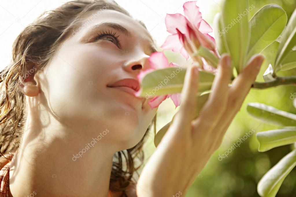 beautiful young woman holding a flower close to her nose