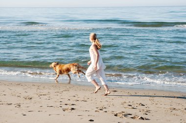 onun golden retriever ile plaj kıyısında sabahın erken sırasında çalışan genç kız.