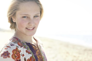 kameraya gülümseyen bir plaj kıyısında duran sarışın bir kızın yakın çekim.