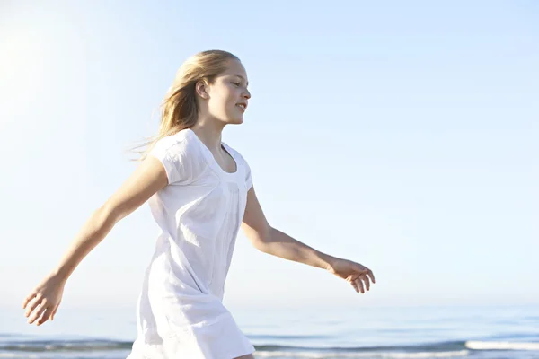 Side view of a girl walking along the shore on a beach with blue sky in the background. — Stock Photo, Image