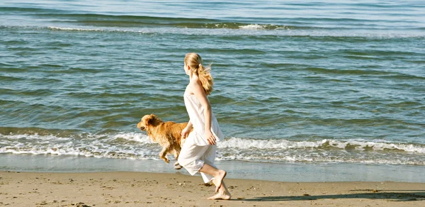 年轻少女与她在海滩沿岸的金毛寻回犬运行. — 图库照片