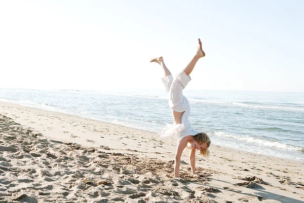 Girl doing cartwheels on a golden sand beach near the shore, smiling happy. — Stock Photo, Image
