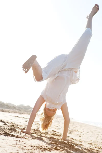 Jong meisje doen cartwheels op een gouden zand strand met de stralen van de zon filteren door middel van haar lichaam tijdens zonsondergang. — Stockfoto