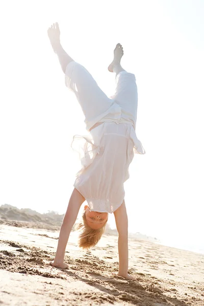 Jong meisje doen cartwheels op een gouden zand strand met de stralen van de zon filteren door middel van haar lichaam tijdens zonsondergang. — Stockfoto