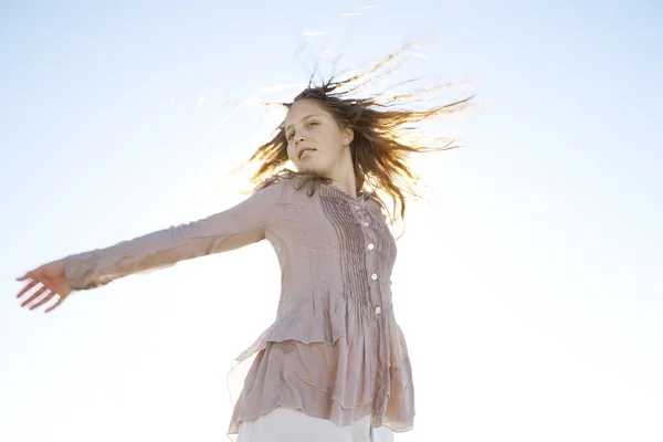 Chica moviendo su cabello contra un cielo azul con los rayos de sol filtrándose a través de su cabello . — Foto de Stock