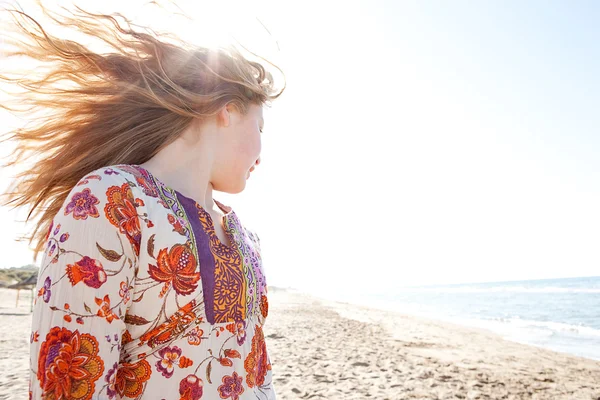 年轻的女孩，她的头发金黄的沙滩上弹与筛选通过她的头发，虽然她微笑的太阳光线 — 图库照片