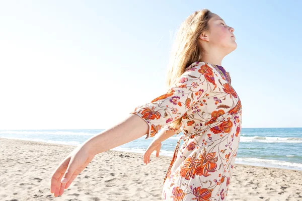 Молодая девушка дышит свежим воздухом, наслаждаясь солнцем на золотом песчаном пляже с голубым небом и морским горизонтом на заднем плане . — стоковое фото