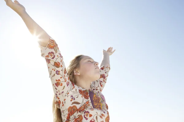 Девушка с распростертыми руками на фоне голубого неба с солнцем, проникающим через ее руку . — стоковое фото