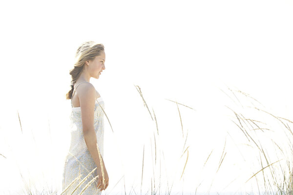 Girl standing with long grass against the open sky at the beach.