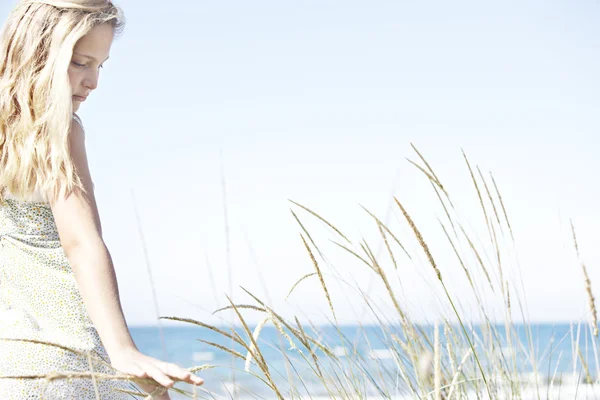 Chica en la playa girando y tocando la hierba larga contra un cielo azul . — Foto de Stock