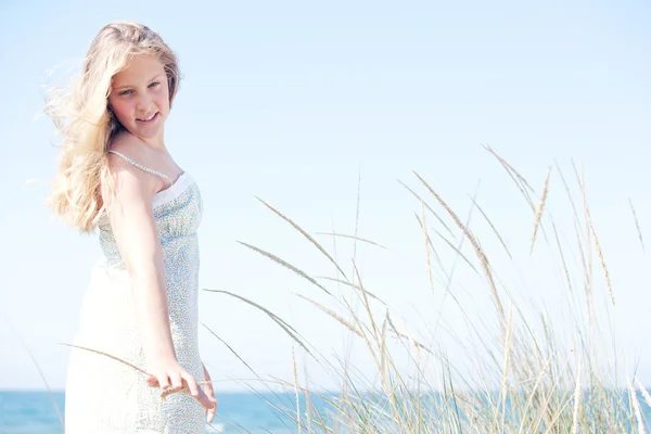 Young girl standing against a blue sky with long grass by the sea